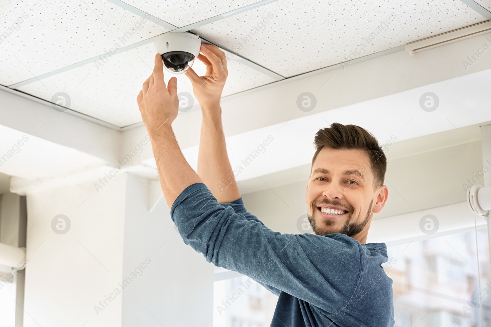 Photo of Technician installing CCTV camera on ceiling indoors