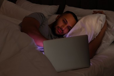 Photo of Young man using laptop in bed at night. Internet addiction