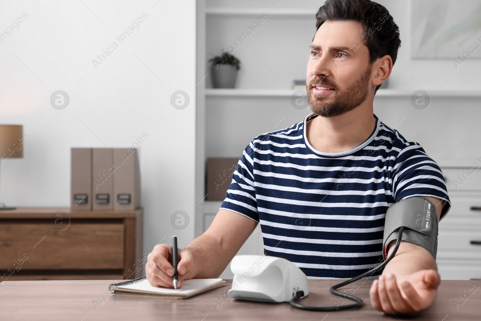 Photo of Man measuring blood pressure and writing it down into notebook in room, space for text