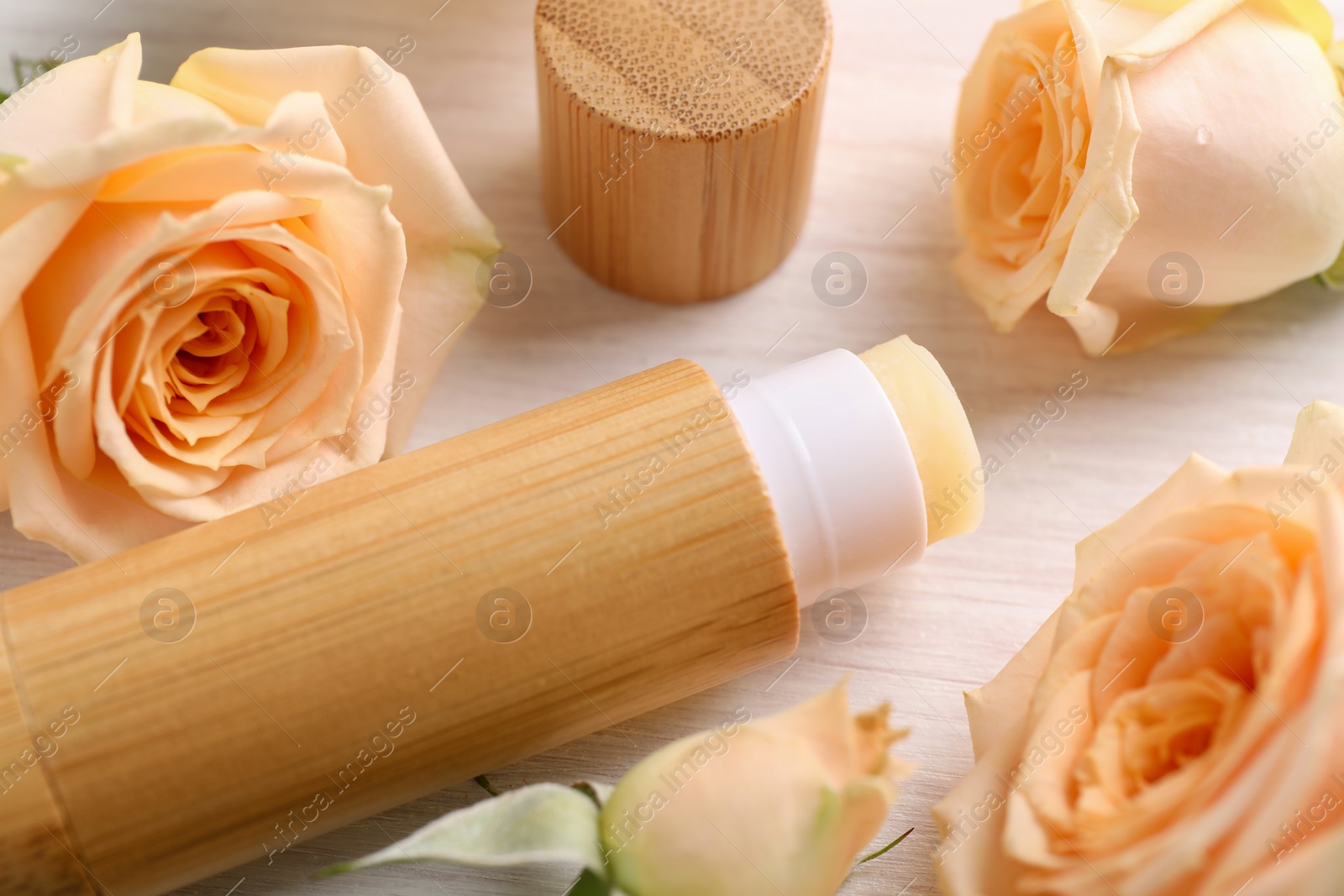 Photo of Lip balm and rose flowers on white wooden background, closeup