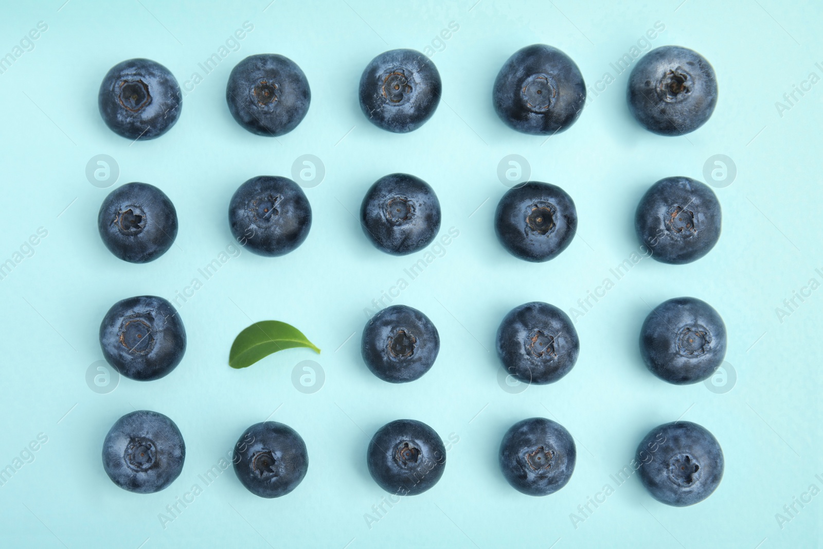 Photo of Fresh ripe blueberries and leaf on light blue background, flat lay