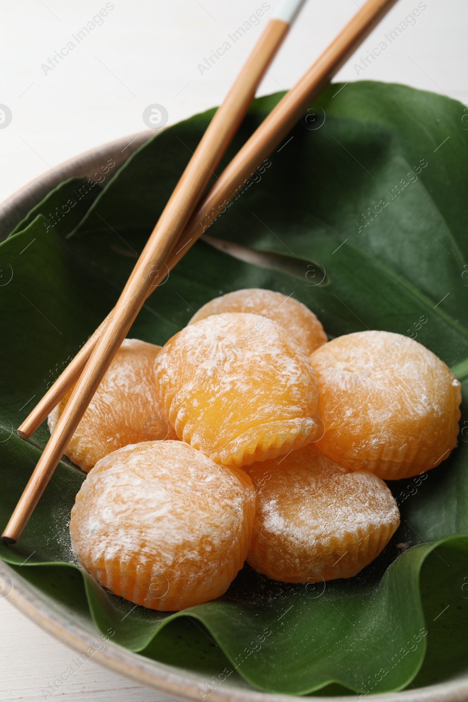 Photo of Delicious mochi served in bowl with green leaf and chopsticks on white table, closeup. Traditional Japanese dessert