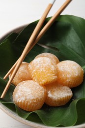 Delicious mochi served in bowl with green leaf and chopsticks on white table, closeup. Traditional Japanese dessert