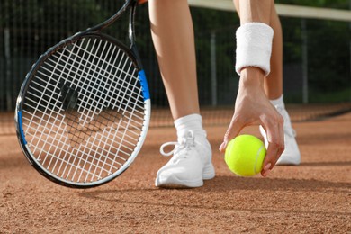 Photo of Young woman with tennis racket and ball at court on sunny day, closeup