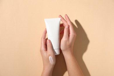 Photo of Woman with tube of hand cream on beige background, top view