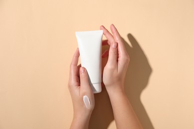 Woman with tube of hand cream on beige background, top view