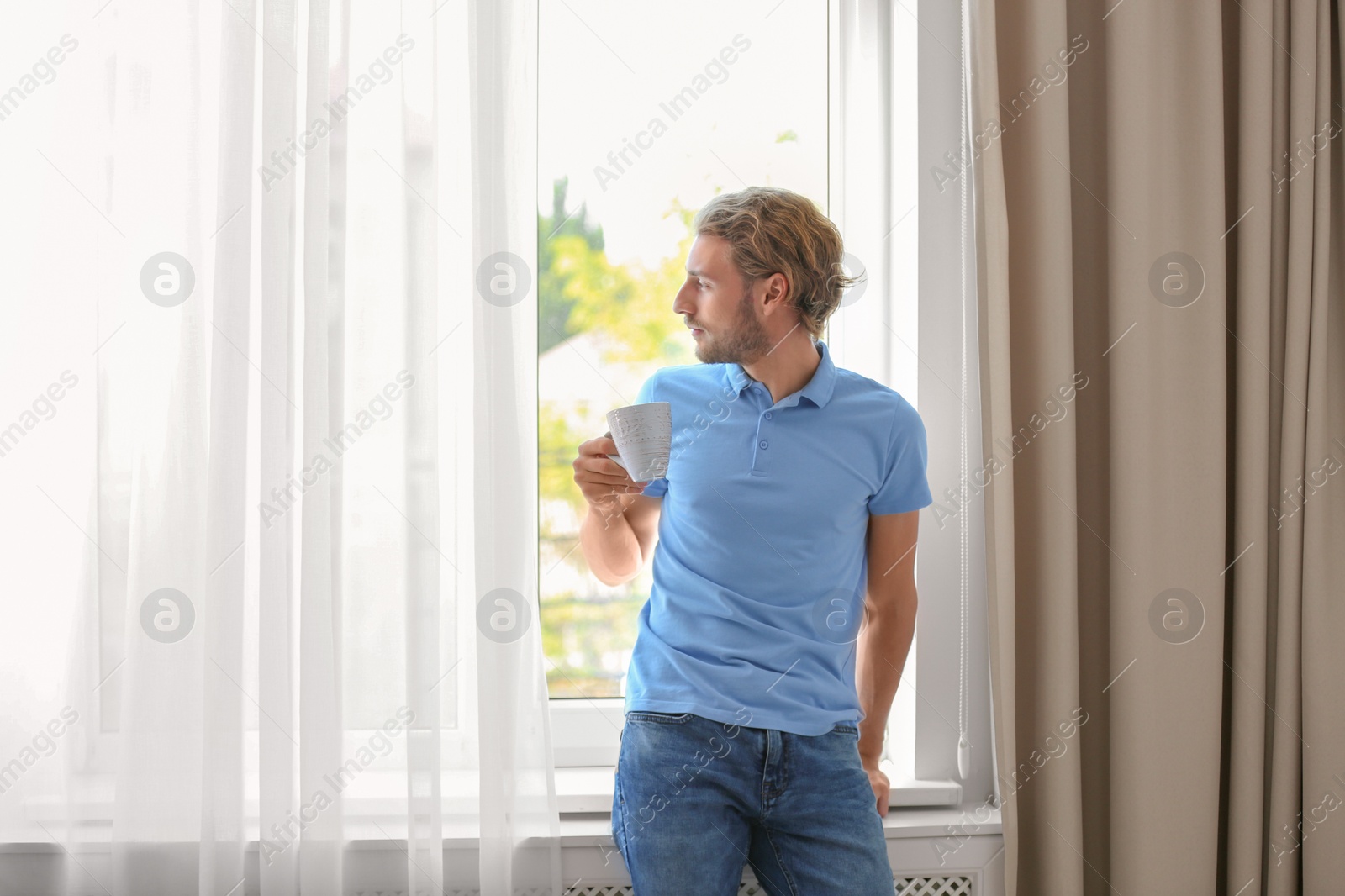 Photo of Young man having rest near window with open curtains at home