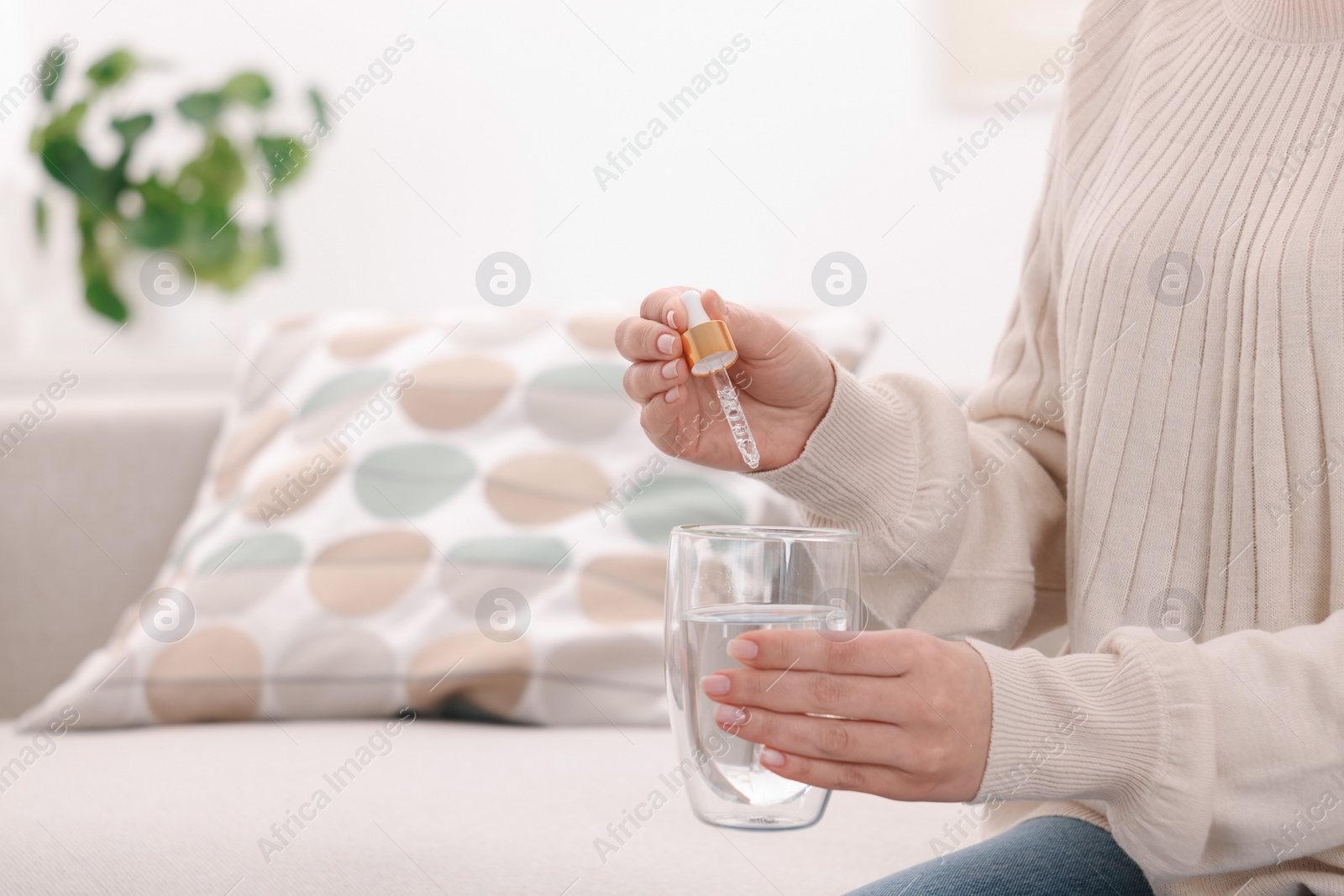 Photo of Woman dripping food supplement into glass of water indoors, closeup. Space for text