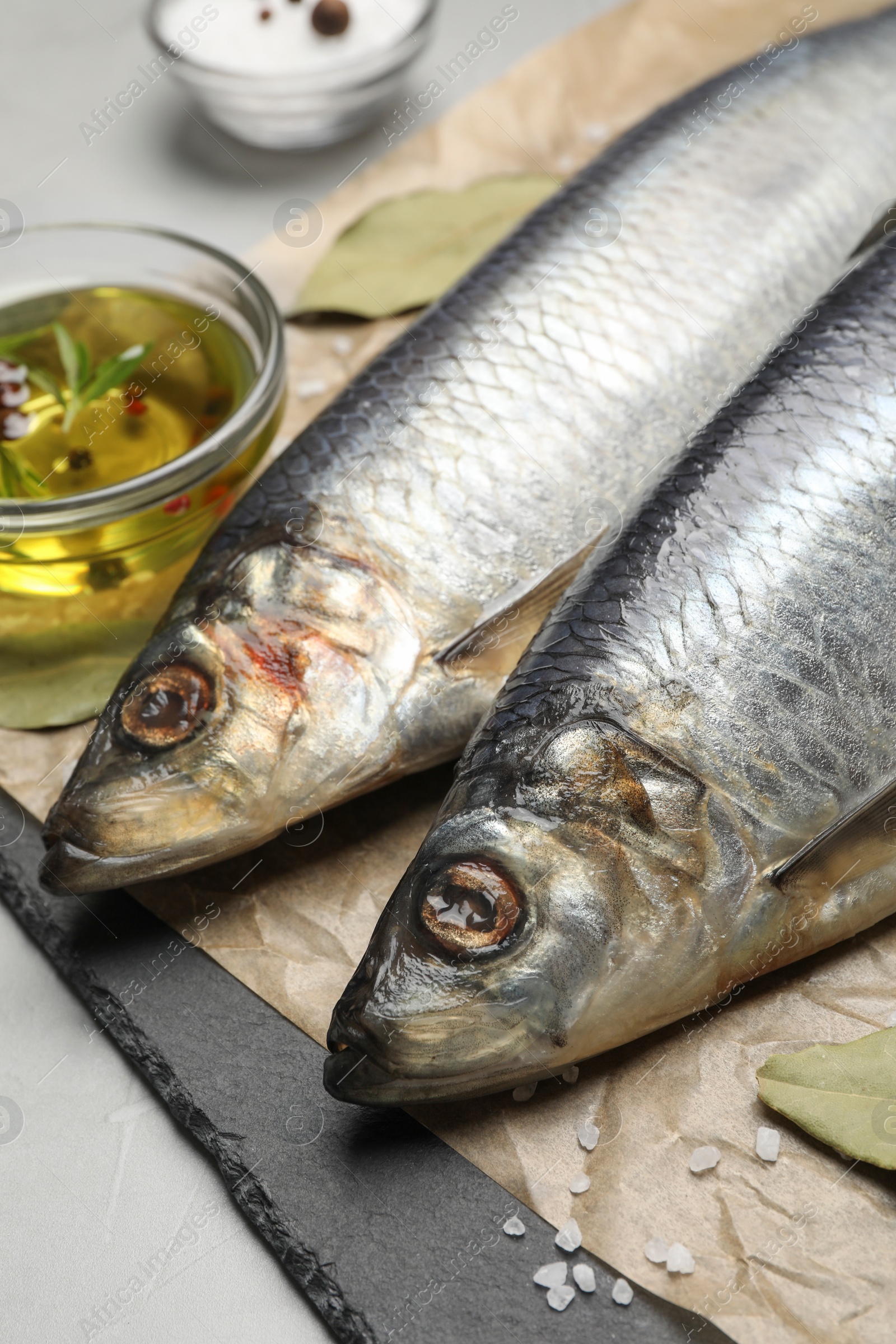 Photo of Slate plate with salted herrings, oil and spices on grey table, closeup