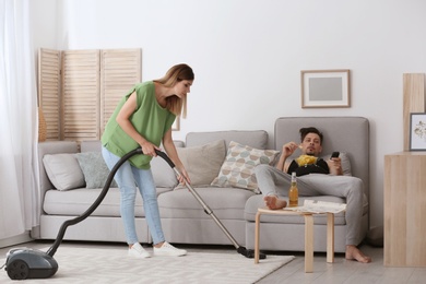 Lazy husband lying on sofa and his wife cleaning at home