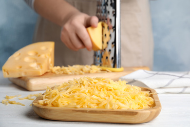 Photo of Woman grating cheese at table, focus on wooden plate