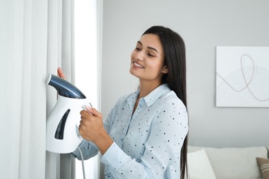 Woman steaming curtain near window at home