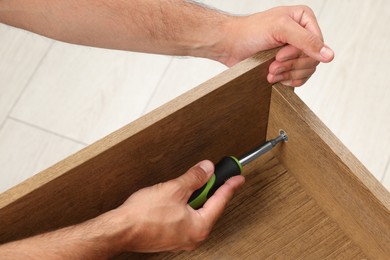 Photo of Man with screwdriver assembling drawer indoors, closeup