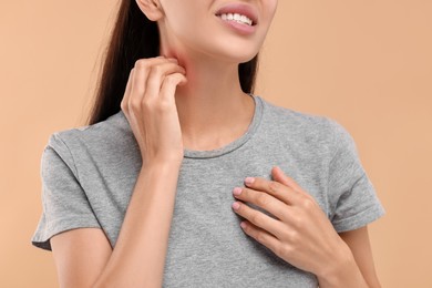 Suffering from allergy. Young woman scratching her neck on beige background, closeup