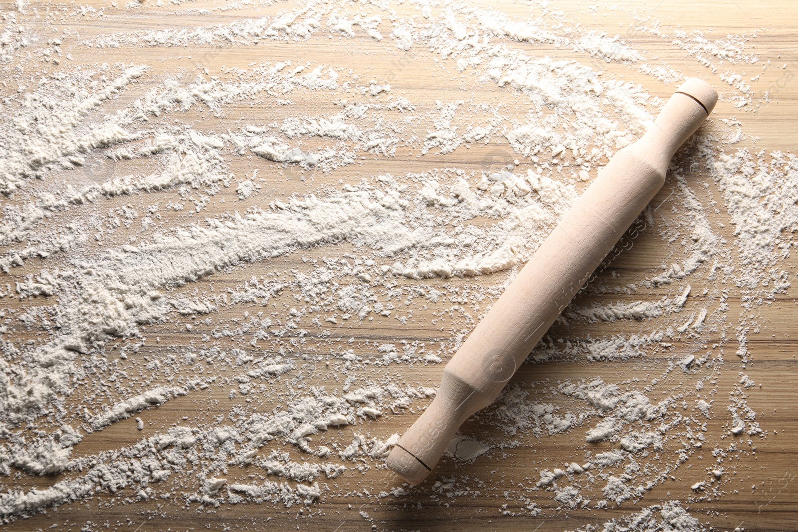 Photo of Scattered flour and rolling pin on wooden table, top view