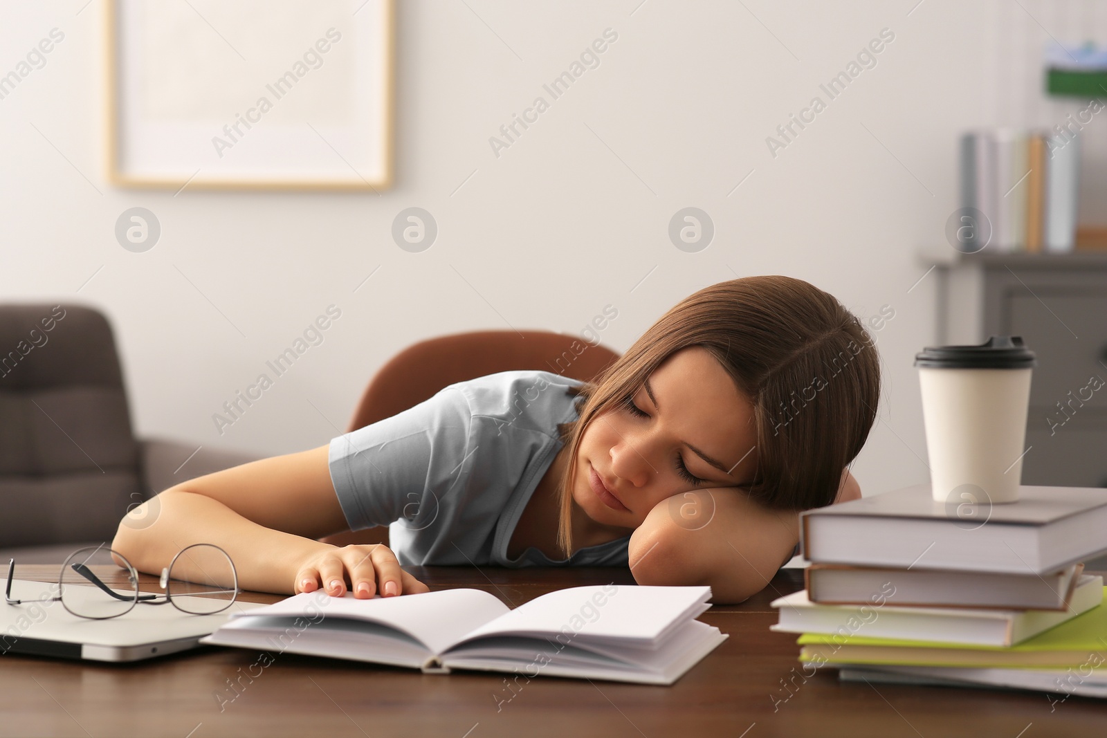 Photo of Young tired woman sleeping near books at wooden table indoors