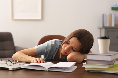 Young tired woman sleeping near books at wooden table indoors