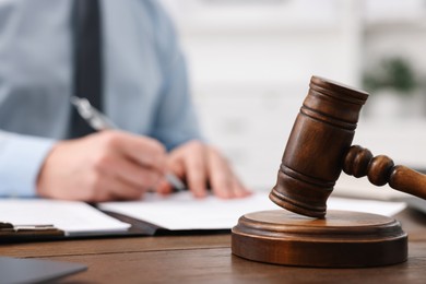 Photo of Lawyer working with documents at wooden table in office, focus on gavel