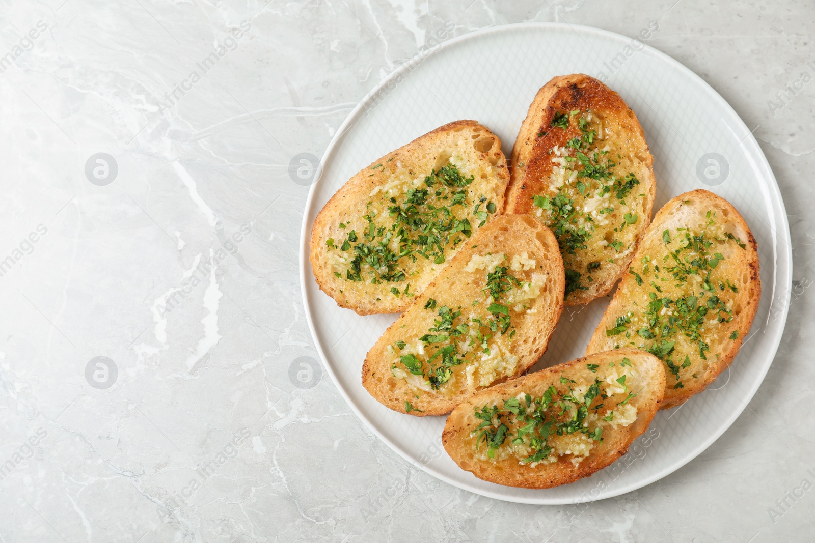 Photo of Slices of toasted bread with garlic and herb on light grey marble table, top view. Space for text