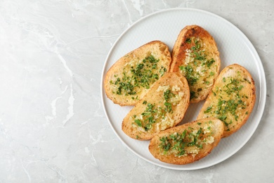 Slices of toasted bread with garlic and herb on light grey marble table, top view. Space for text