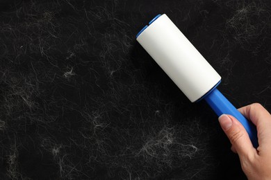 Woman with lint roller removing pet hair from black fabric, top view. Space for text