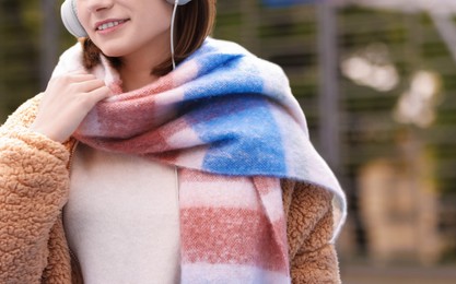 Photo of Beautiful woman in warm scarf listening to music outdoors, closeup