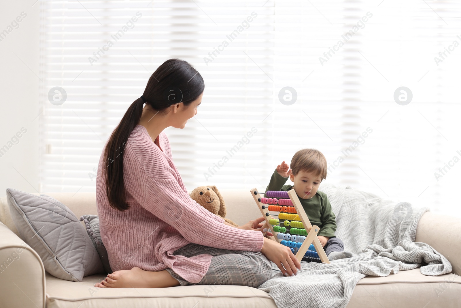 Photo of Young nanny and cute little baby playing with abacus at home