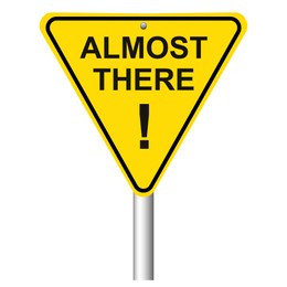 Yellow road sign with phrase Almost There and exclamation mark on white background