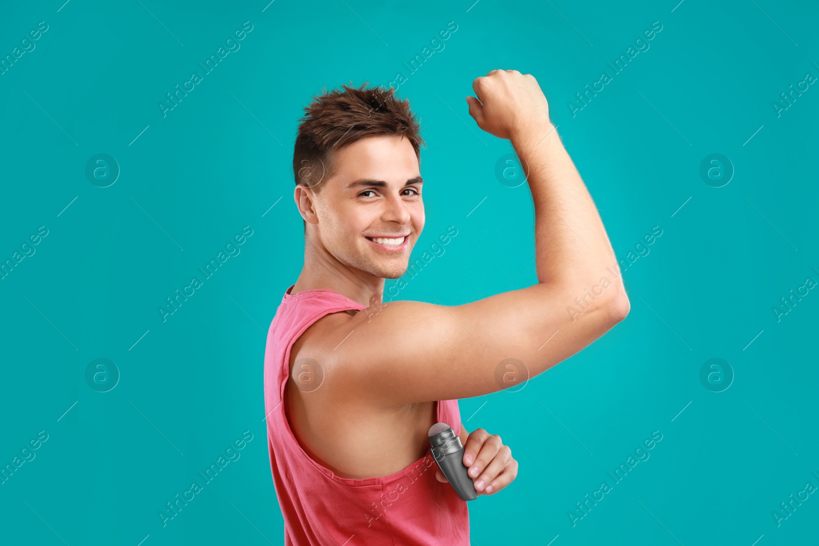 Photo of Young man applying deodorant to armpit on blue background