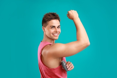 Young man applying deodorant to armpit on blue background