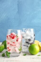 Photo of Glasses of drinks with fruit ice cubes on table against color background. Space for text