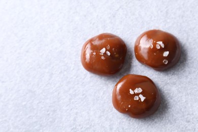 Tasty caramel candies and salt on light grey table, top view. Space for text