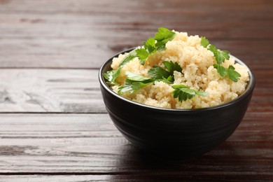 Photo of Tasty quinoa porridge with parsley in bowl on wooden table, closeup. Space for text