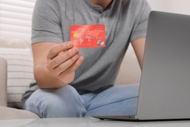 Man with credit card using laptop for online shopping at home, closeup