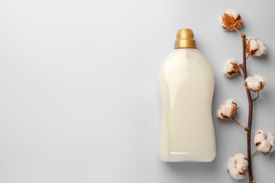 Photo of Bottle of fabric softener and branch with fluffy cotton flowers on light background, flat lay. Space for text