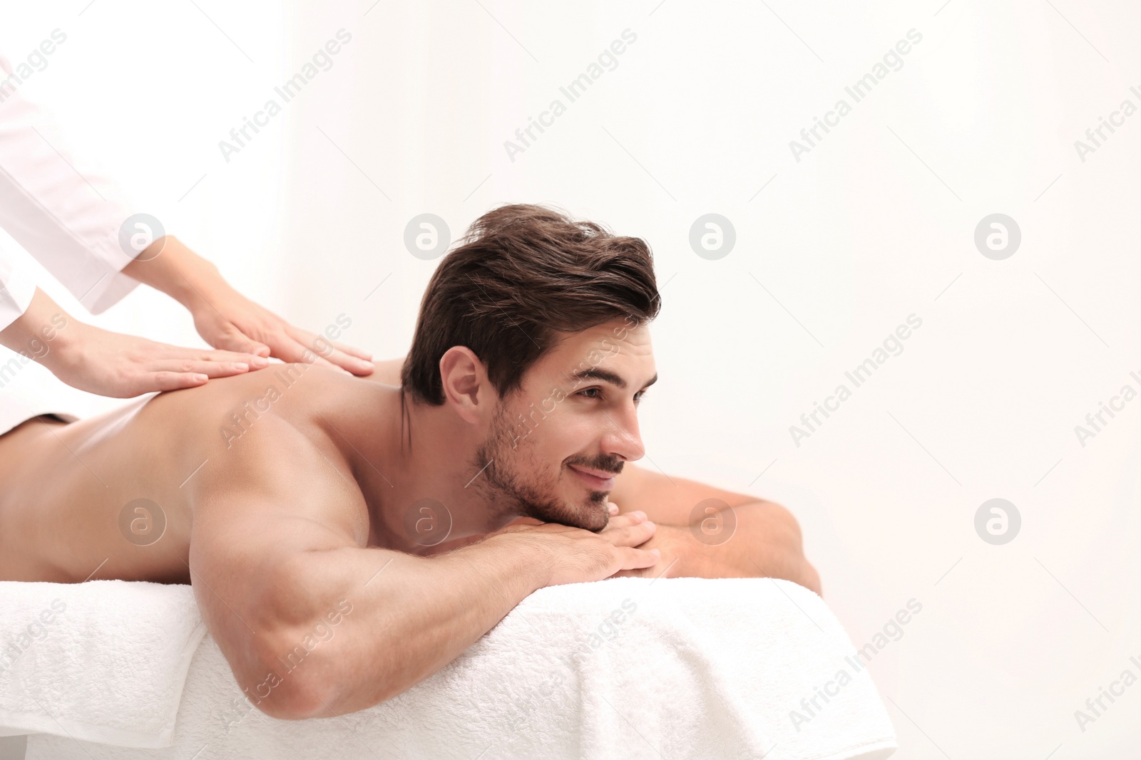 Photo of Handsome young man receiving back massage on light background, space for text. Spa salon