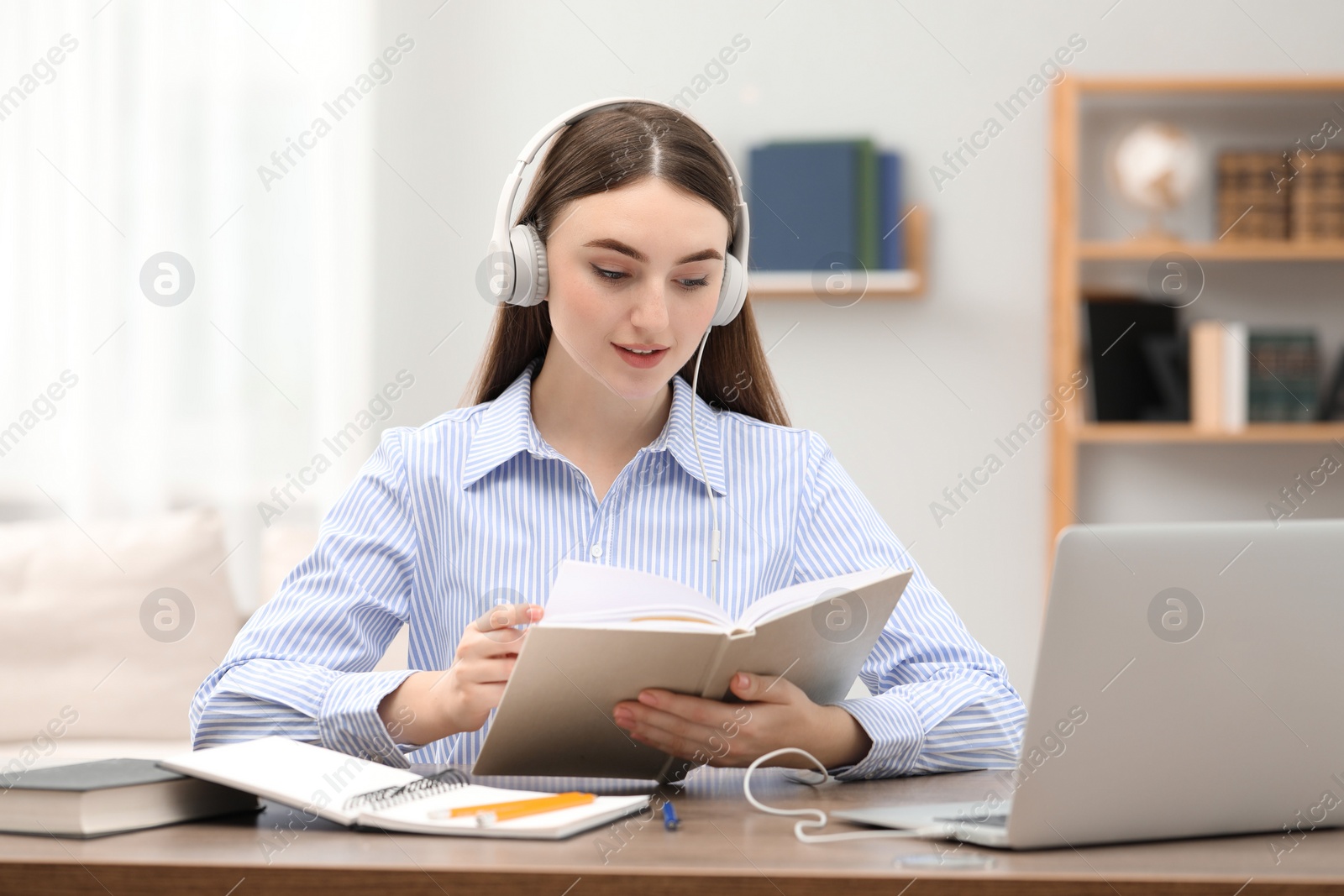 Photo of E-learning. Young woman with book during online lesson at table indoors