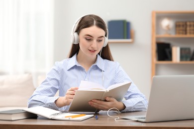 E-learning. Young woman with book during online lesson at table indoors