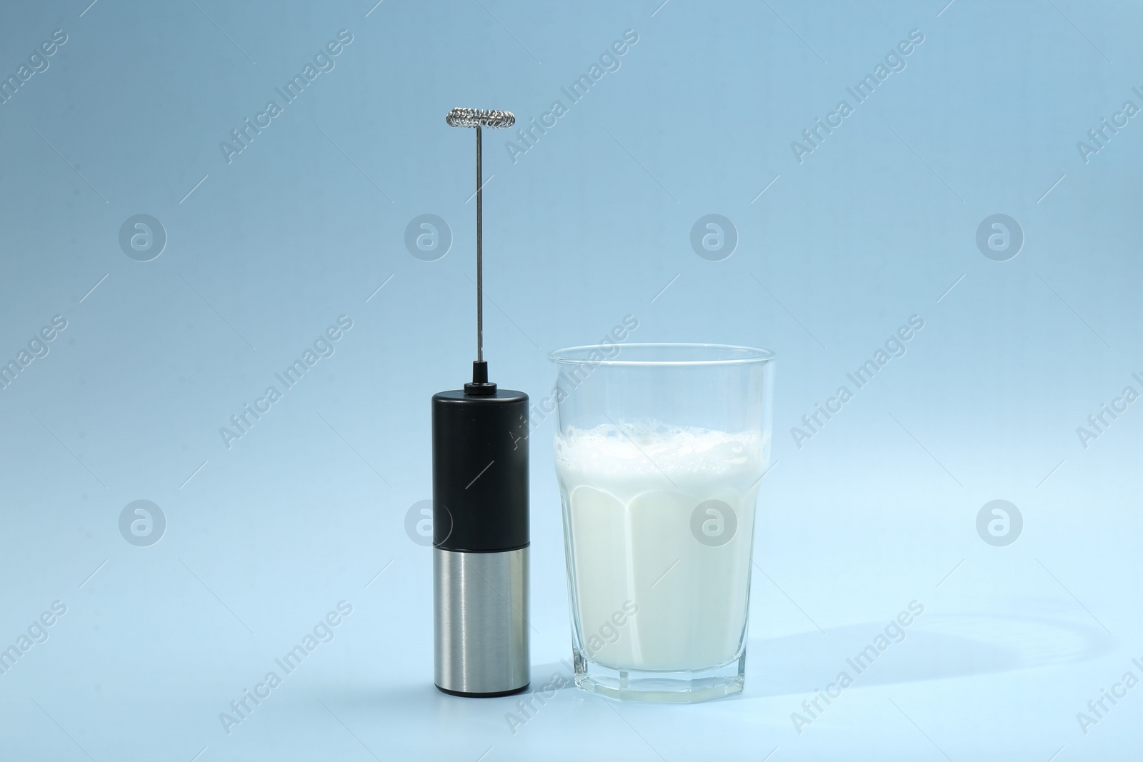 Photo of Mini mixer (milk frother) and whipped milk in glass on light blue background