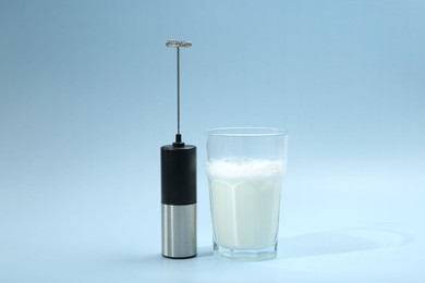 Photo of Mini mixer (milk frother) and whipped milk in glass on light blue background