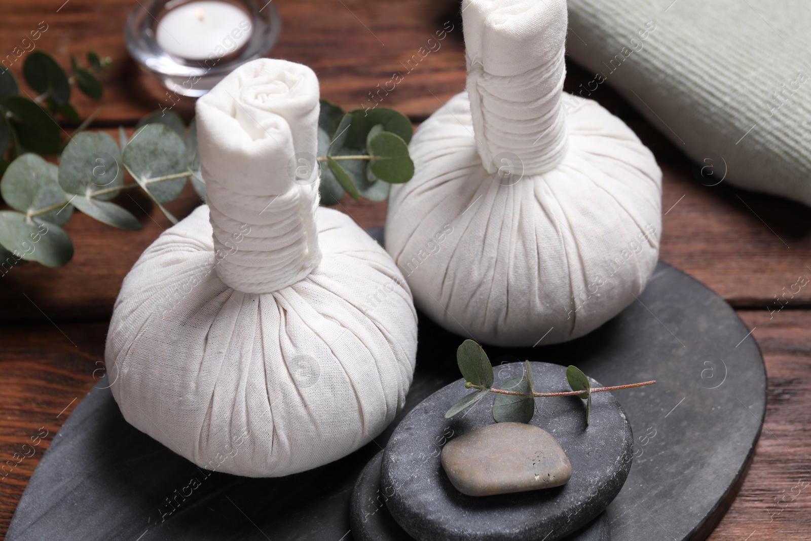 Photo of Beautiful spa composition with herbal massage bags, stones and eucalyptus branches on wooden table