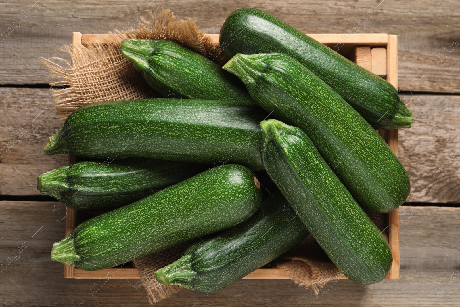 Photo of Raw ripe zucchinis in crate on wooden table, top view