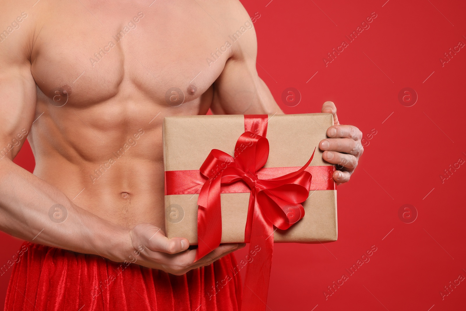 Photo of Young man with muscular body holding Christmas gift box on red background, closeup