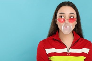 Beautiful young woman blowing bubble gum on light blue background. Space for text