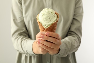 Woman holding green ice cream in wafer cone on light background, closeup