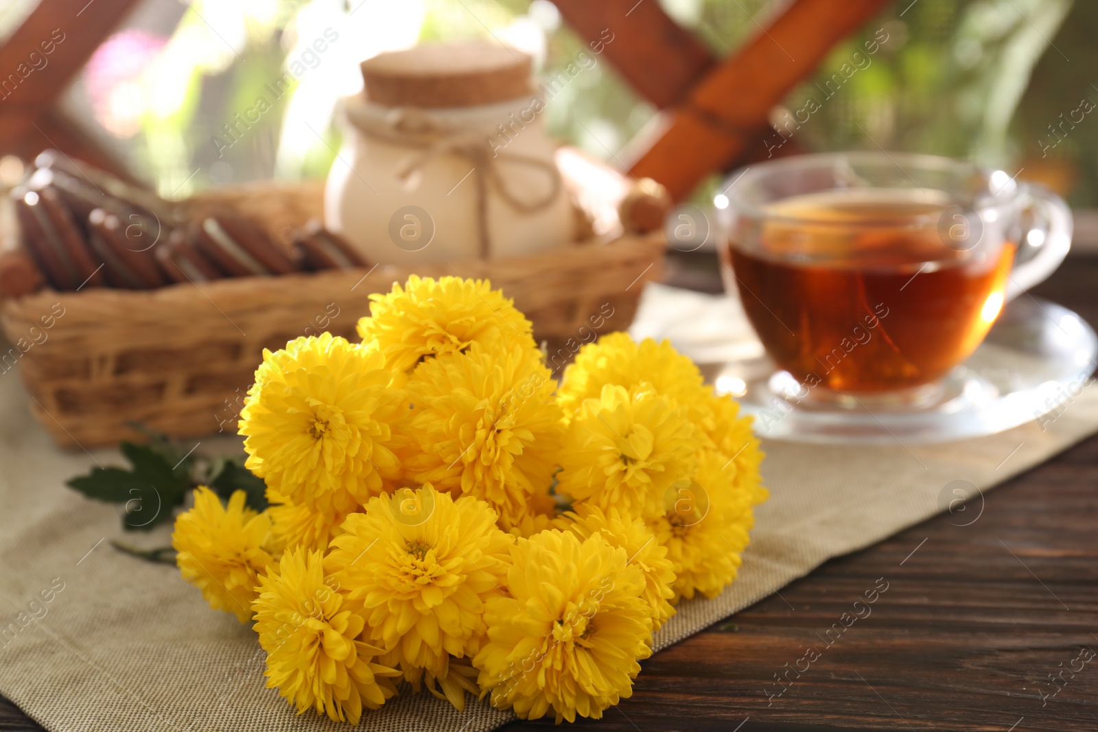 Photo of Beautiful yellow chrysanthemum flowers, cup of aromatic tea and sweet chocolate treats on wooden table