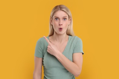 Surprised woman pointing at something on yellow background