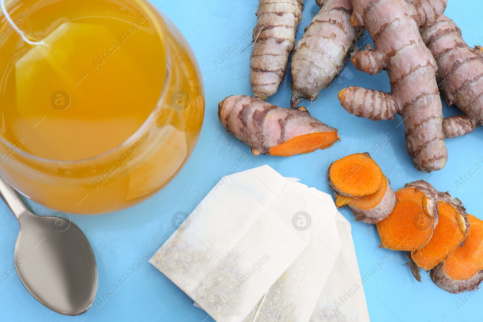 Photo of Glass cup with hot tea and turmeric roots on light blue tray, above view