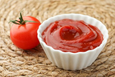 Photo of Bowl of tasty ketchup and tomato on wicker mat, closeup