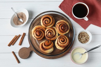 Tasty cinnamon rolls and ingredients on white wooden table, flat lay